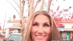 Blondine lächelt in heller Küche, rotes Logo hinter ihr