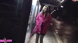 Frau in rosa Mantel steht nachts an Haltestelle