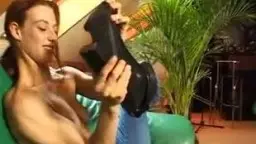 Rothaarige Frau sitzt nackt auf grünem Sofa, Beine gespreizt.