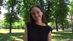 Gina mit rotbraunem Haar sitzt schüchtern lächelnd auf einer sonnigen Parkbank