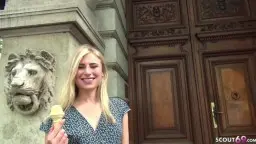 Blonde Linday in blauem Kleid lächelt mit Eis in der Hand vor klassischer Hausfassade
