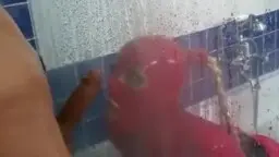 Mann mit Gasmaske und blankem Oberkörper steht unter der Dusche, während eine rote Latex-Gummipuppe vor ihm kniet.