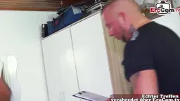 Tätowierter Mann mit Glatze steht in schwarzem Shirt in weißem Zimmer und schaut auf dünne nackte Svenja herunter.