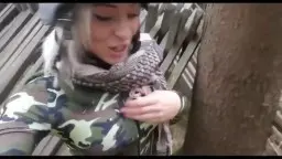 Blonde Frau kniet im Camouflage-Jackett vor Baum, nimmt Schwanz in den Mund