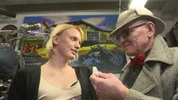 Blonde Frau kniet vor älterem Mann in Werkstatt
